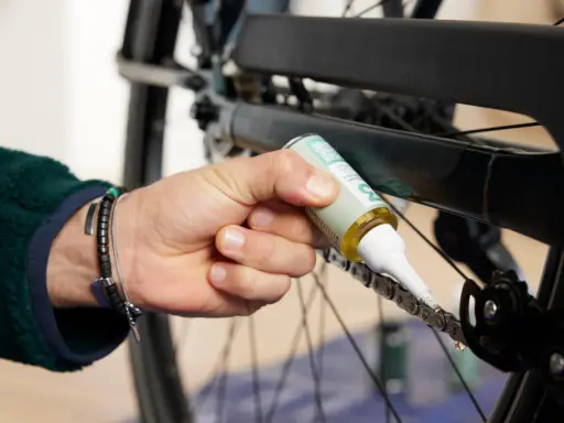 Dłoń z buteleczką oleju aplikuje go na rowerowy łańcuch, dbając o jego płynne działanie. Czyszczenie łańcucha rowerowego to klucz do sprawnej jazdy.