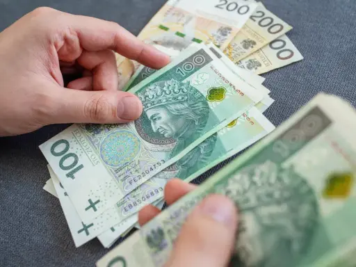 Ręce liczą polskie banknoty 100 zł i 200 zł. Zastanawiasz się, ile wynosi renta rodzinna?