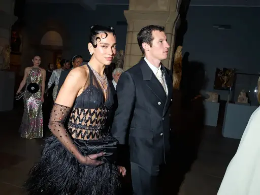 Dua Lipa stuns at the Met Gala in a black feathered gown and diamond necklace, walking with a companion.