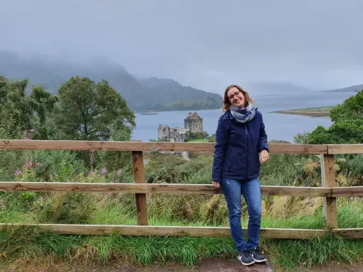 Frau vor schottischer Burg bei typischem Septemberwetter. Die Landschaft ist grün, das Wetter schottland september ist wechselhaft, aber die Stimmung ist gut.