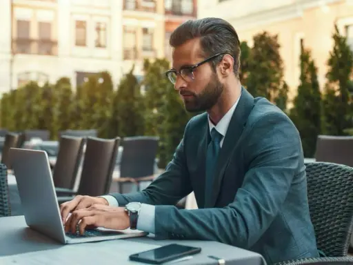 Mężczyzna w garniturze pracuje na laptopie w kawiarni. Jego kod zawodu to prawdopodobnie coś związanego z biznesem.