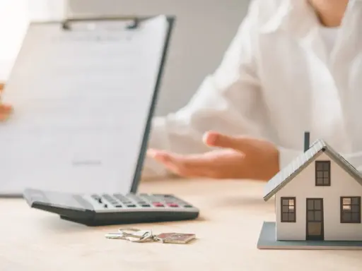 Une personne présente un contrat, une calculatrice, des clés et une maquette de maison. L'ambiance est un peu sinistre, comme si un problème était sur le point d'être révélé.