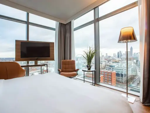 Modern Hotelzimmer mit Skyline-Blick, Bett, Sessel und Fernseher.