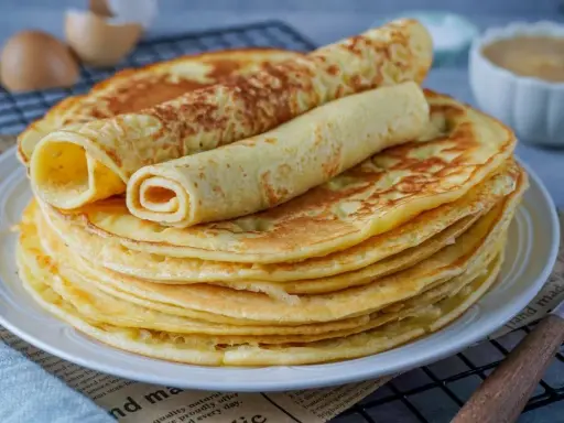 Ein Stapel goldbrauner Eierkuchen, zwei davon gerollt, perfekt für ein einfaches Eierkuchen Rezept.