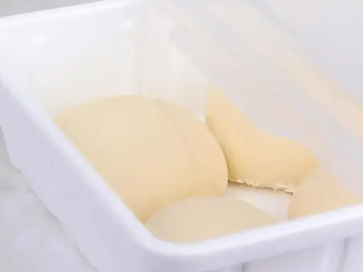 Pâte à pain trop fermenté dans une boîte blanche, prête pour la cuisson.