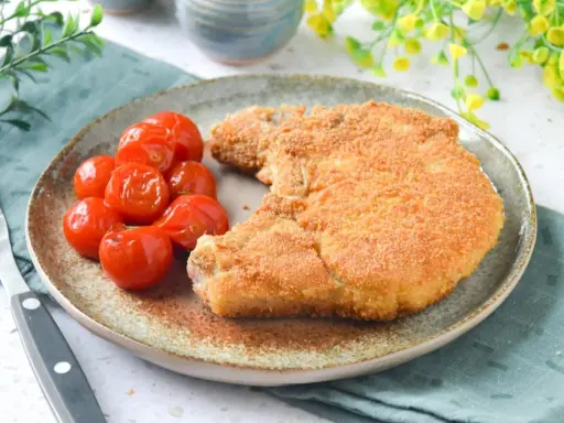Cotoletta alla milanese dorada y crujiente, acompañada de tomates cherry asados. Un plato clásico y delicioso.