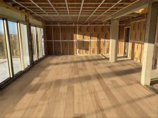Pose de parquet clair dans une pièce en construction, le sens des lames semble agrandir l'espace.