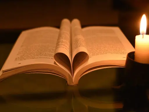 Otwarta księga z kartkami uformowanymi w serce, obok płonąca świeca. W świetle świecy czytam psalm 37 1-4.