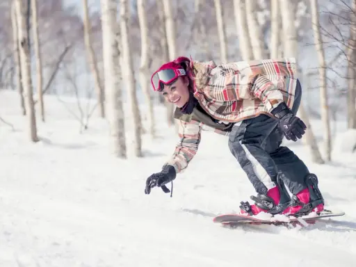 Uśmiechnięta snowboardzistka z różowymi włosami zjeżdża po ośnieżonym stoku wśród drzew. To świetna zabawa podczas chodzenia po górach zimą.