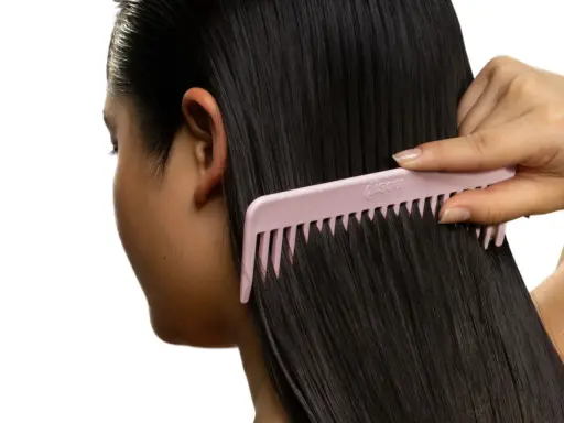 Une main peigne des cheveux noirs et brillants avec un peigne rose. Le peigne est large et espacé, idéal pour démêler les cheveux sans les casser, évitant ainsi les cheveux emmêlés cause.