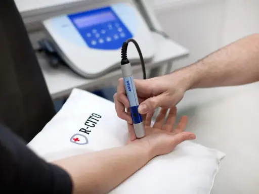 Fizjoterapeuta wykonuje zabieg laserem na dłoni pacjenta.