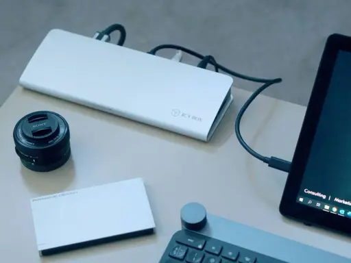 Stacja dokująca ICY BOX podłączona do laptopa, obok obiektyw Sony i dysk Porsche Design.