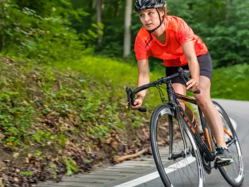 Frau im Helm fährt Rad auf einer Straße im Wald. Sie bereitet sich auf die triathlon sprintdistanz vor.