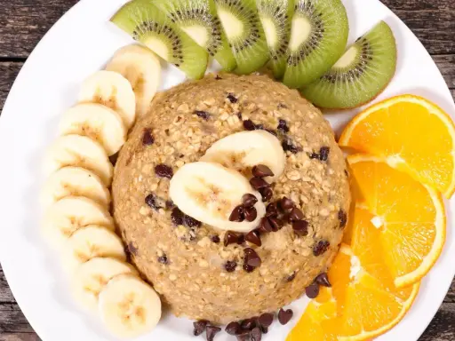 Un délicieux bowl cake flocon d'avoine, garni de rondelles de banane, de tranches de kiwi et d'orange, parsemé de pépites de chocolat.