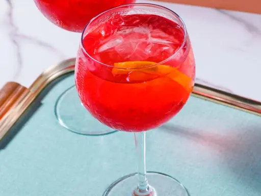 Ein erfrischender Campari Spritz mit Eis und Orangenscheibe auf einem Tablett.
