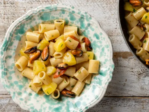 Un piatto di pasta patate e cozze, un classico della cucina italiana, servito in una ciotola decorata.
