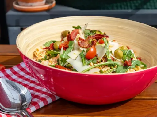Leckere nudelsalat ideen: Pasta mit Rucola, Tomaten, Oliven und Parmesan in einer roten Schüssel.