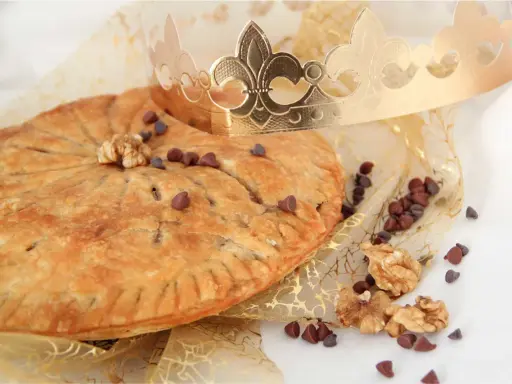 Une galette des rois pépite de chocolat dorée, parsemée de pépites de chocolat et de noix, sous une couronne royale.