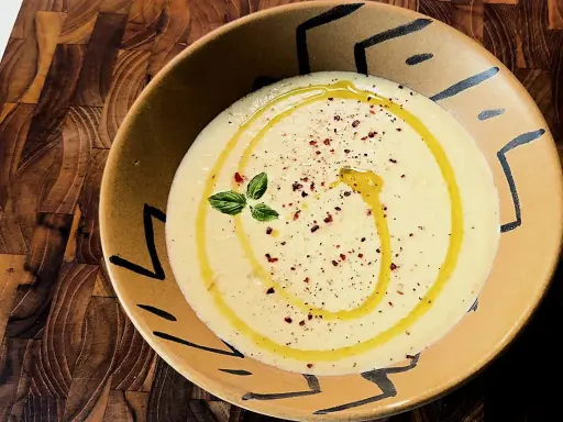 Gazpacho de calabacín cremoso, con un hilo de aceite de oliva, pimentón y una ramita de albahaca, servido en un cuenco artesanal.