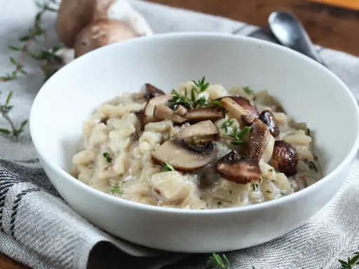 Aksamitne risotto z pieczarkami, udekorowane świeżym tymiankiem, w białej misce na lnianej serwetce.
