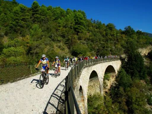 Ciclisti in gruppo percorrono la ciclabile Spoleto Norcia su un viadotto panoramico, immersi nel verde.