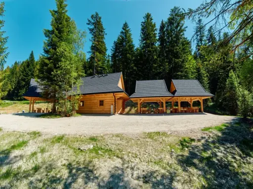 Drewniana bacówka w górach, otoczona lasem. Dwa zadaszone tarasy z drewnianymi stołami i ławami zapraszają do odpoczynku.
