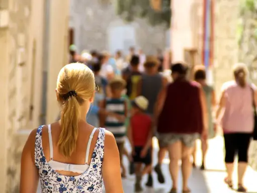 Kobieta z blond kucykiem idzie wąską uliczką pełną ludzi, odkrywając urokliwe villach atrakcje.