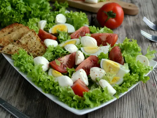 Sałatka z mozzarellą, pomidorami, jajkiem i grzankami na białym talerzu.
