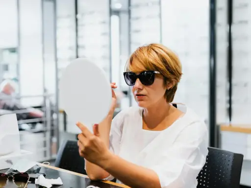 Kobieta w okularach do noszenia na co dzień przymierza nowe okulary w salonie optycznym, patrząc w lusterko.