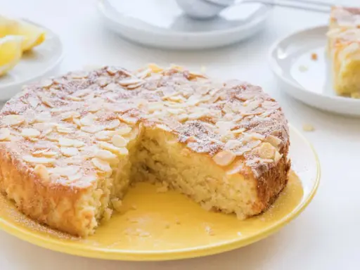 Ein köstlicher Zitronen-Mandelkuchen, perfekt für rezepte mit mandelmehl. Mit Mandelblättchen und Puderzucker bestreut, daneben frische Zitronenspalten.