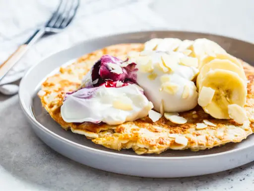 Puszysty omlet z jogurtem, jagodami, bananem i płatkami migdałów. Idealny przepis na zdrowy omlet na śniadanie.