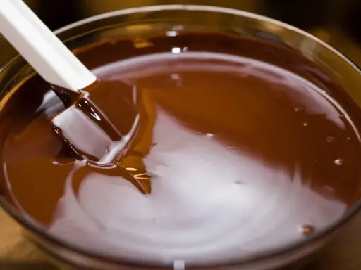 Spatule blanche remuant du chocolat fondu dans un bol en verre. Le chocolat est lisse et brillant, prêt à être utilisé pour une recette.
