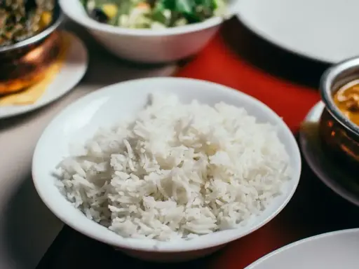 Biały ryż, źródło węglowodanów, w misce obok indyjskiego curry i sałatki.