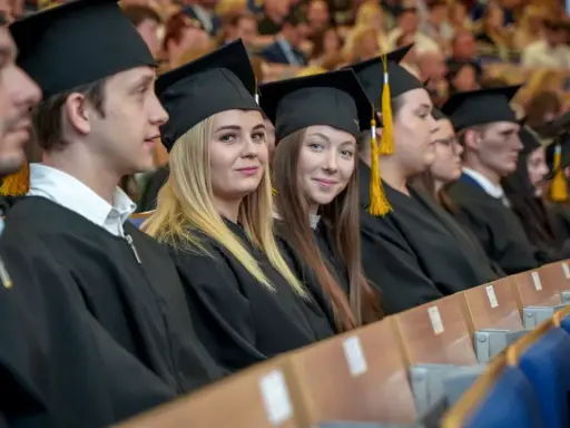 Absolwenci w togach i biretach siedzą w rzędach, gotowi do odbioru dyplomów. Uczelnie Katowice świętują sukcesy studentów.