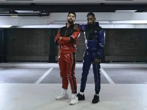 Two gay men in matching red and blue sportswear pose in a parking garage.