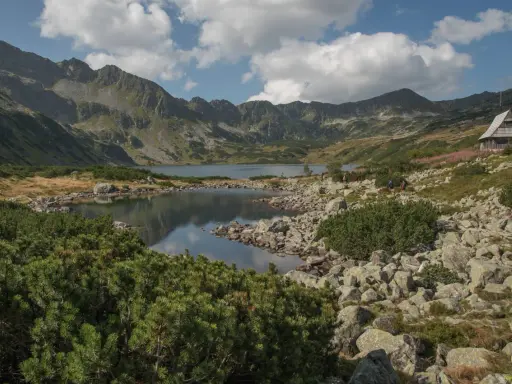 Malownicza dolina Roztoki z jeziorem i górami w tle. Drewniana chata górska na zboczu, kamieniste wybrzeże i kosodrzewina.