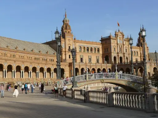 Familien genießen einen sonnigen Tag auf der Plaza de España in Sevilla. Kinder lachen, während sie über die Brücke spazieren, die über einen Kanal führt.