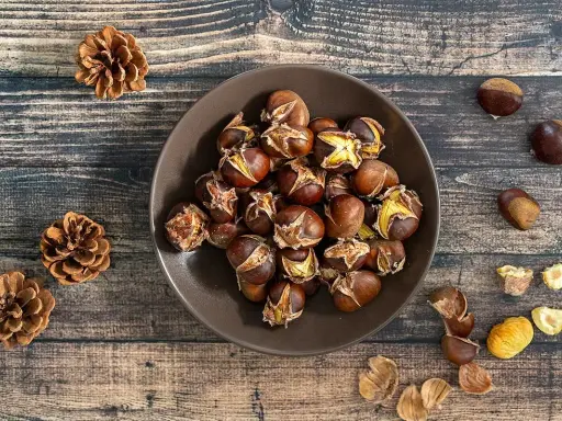 Châtaignes grillées dans un bol, sur fond de bois, avec des pommes de pin.