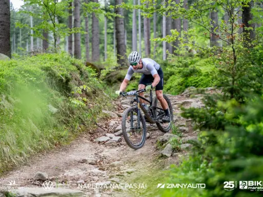 Kolarz MTB pokonuje kamienisty zjazd w lesie. To fragment kalendarza MTB, pełnego adrenaliny i pasji.