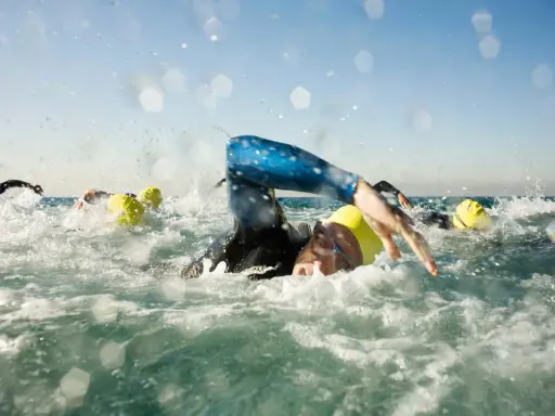 Schwimmer mit gelben Kappen kämpfen sich durch die Wellen. Die triathlon strecken sind anspruchsvoll.