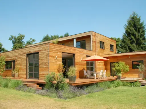 Maison moderne en bois avec terrasse et jardin. La construction maison ossature bois met en valeur le matériau naturel.