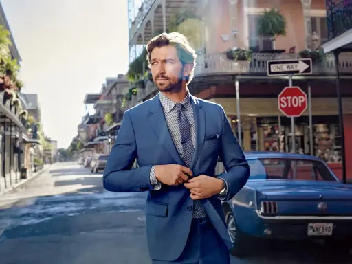 Man in a sharp blue suit, ready for a business cocktail, stands on a street with a vintage car and classic architecture.