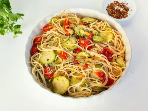 Pyszny makaron z cukinii, pomidorkami i parmezanem, gotowy do podania.