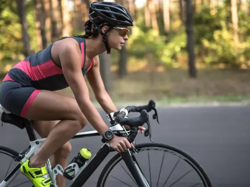 Kobieta w kasku i okularach jedzie na rowerze szosowym przez las. Codzienna jazda na rowerze - efekty widać w jej skupieniu i sportowej sylwetce.