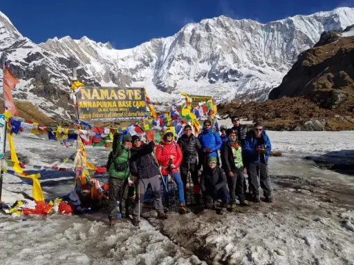 Grupa turystów na tle Annapurny podczas trekking w Nepalu. W tle majestatyczne, ośnieżone szczyty i kolorowe flagi modlitewne.
