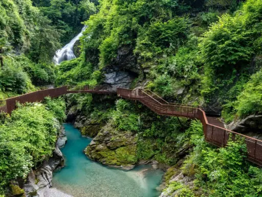 Sentiero panoramico tra gole e cascate, un esempio di posti strani da visitare in Italia, con passerelle in metallo che si snodano tra la vegetazione lussureggiante.
