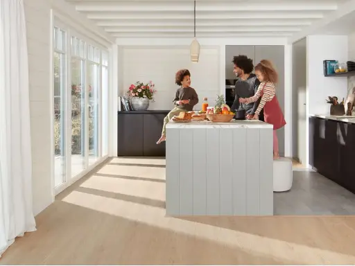 Une famille prépare un repas dans une cuisine moderne. La **délimitation sol cuisine salon** est subtile, avec un parquet clair contrastant avec le carrelage du salon.