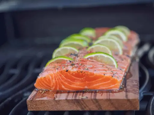 Lachs auf Zedernholz grillen, mit Limettenscheiben und Kräutern belegt. Ein saftiges Stück Fisch auf dem Rost.