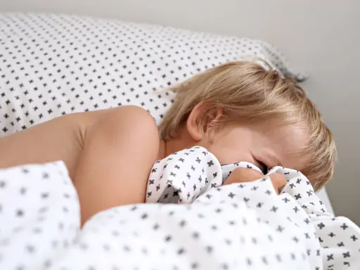 Niño rubio se esconde bajo la sábana. Aprende como hacer que un niño duerma solo con paciencia y rutinas.