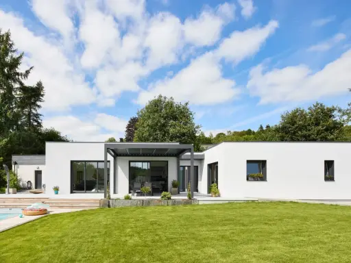 Une maison modulable moderne avec piscine et jardin luxuriant, sous un ciel bleu éclatant.
